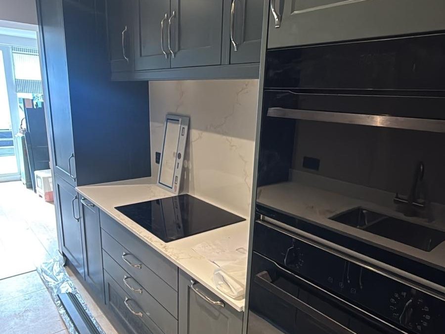 Dark shaker kitchen with a white worktop, induction hob and built in ovens