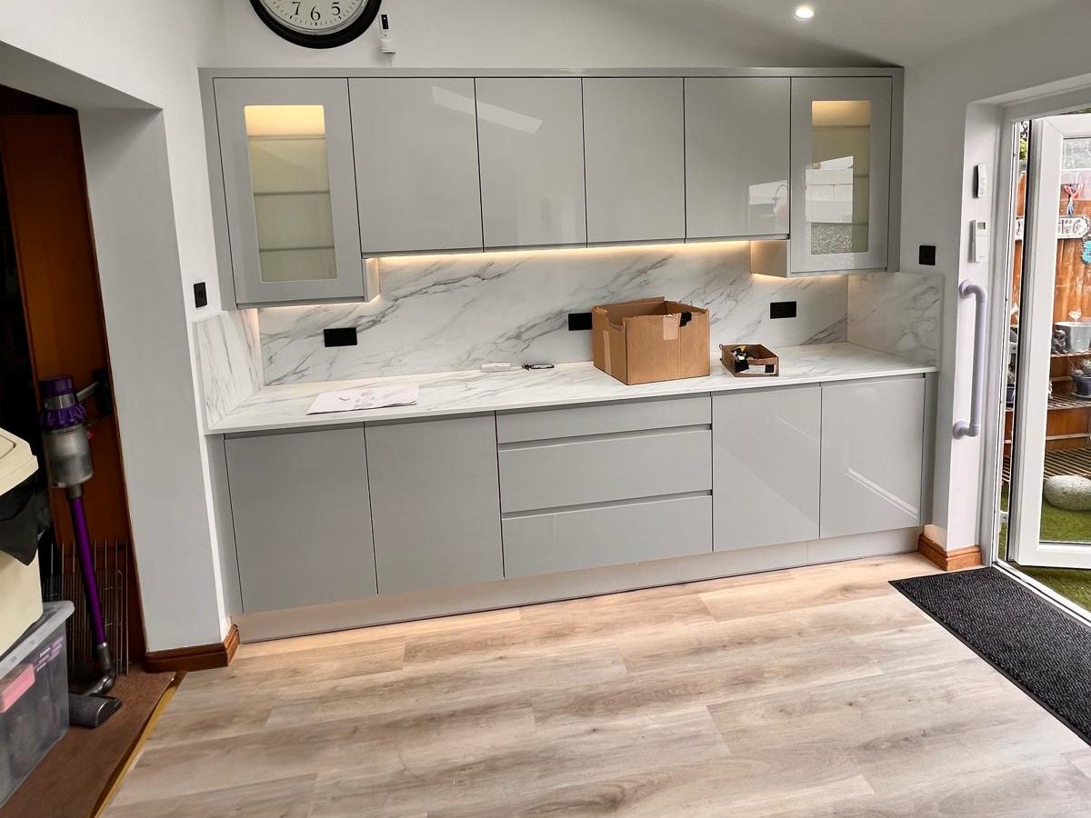 Grey gloss kitchen with a marble effect splashback and lit glazed cabinets